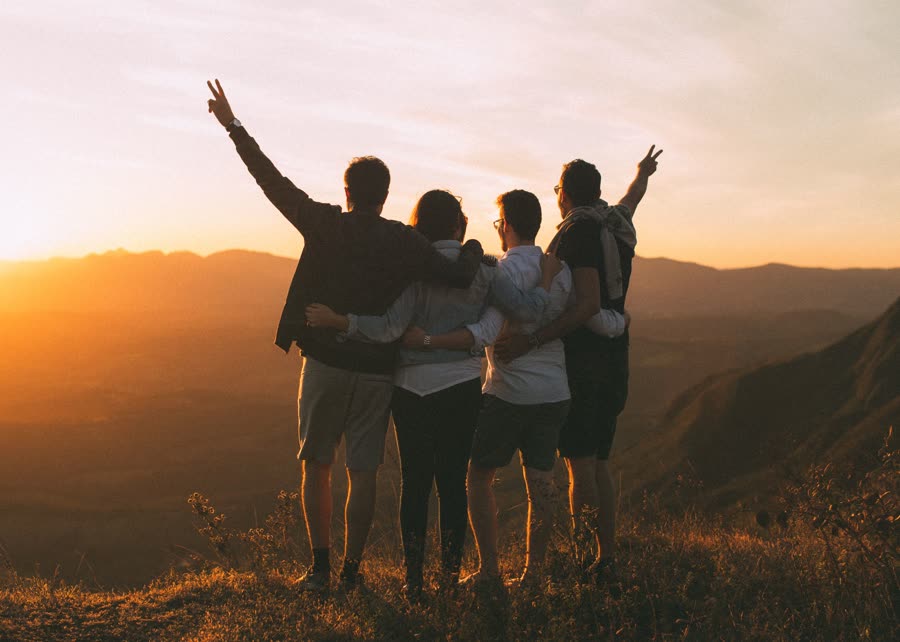 Friends arm in arm on a hilltop at sunset